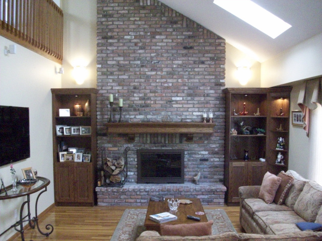 Wall Sconces over Lighted Custom Cabinetry with Corner Curio, Custom Mantel with Hand Carved Corbells, Custom Color Glass Doors and Matching Log Holder with Tool Set, Rebricked Hearth Extention.