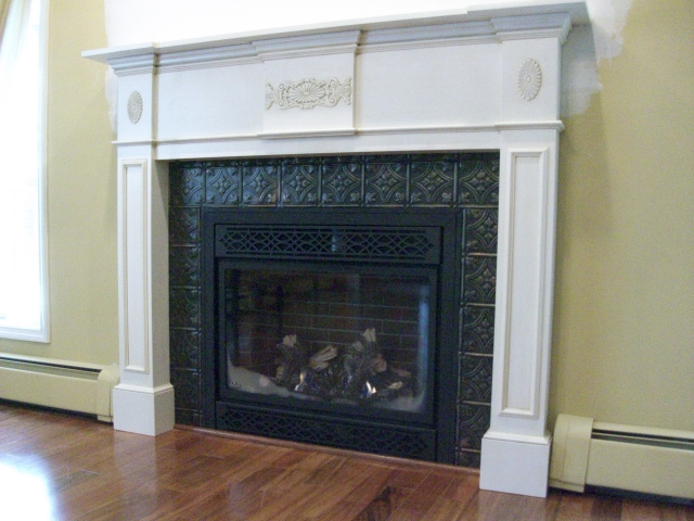 A new gas firebox with ornamental grills, realistic logs and glowing fire, surrounded by hand painted artisan tins, wrapped in a beautiul custom designed period mantel in mayonase color with a light tea glaze. 