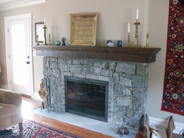 A complete renovation of a woodburning fireplace inside and out. New firebrick firebox with larger opening, reconstructed natural stone facing with decorative border and keystone, custom oak mantel in dark walnut, wrought iron glass doors with aztec inlay design and bluestone hearth slab.