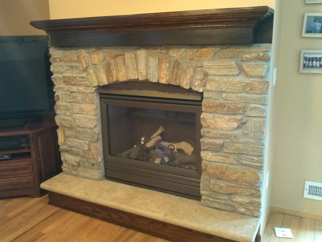 Gas Fireplace with complete new thermostatic remote controlled operating system for off the grid emergency use, goldenfire brown custom colored firebox, natural quarry stone with gentle arch, limestone hearth extention and hand rubbed red mahogany riser & mantel shelf.